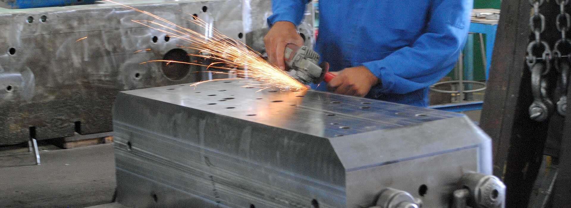 Screen shows a toolmaker using an angle grinder to remove steel from a work piece